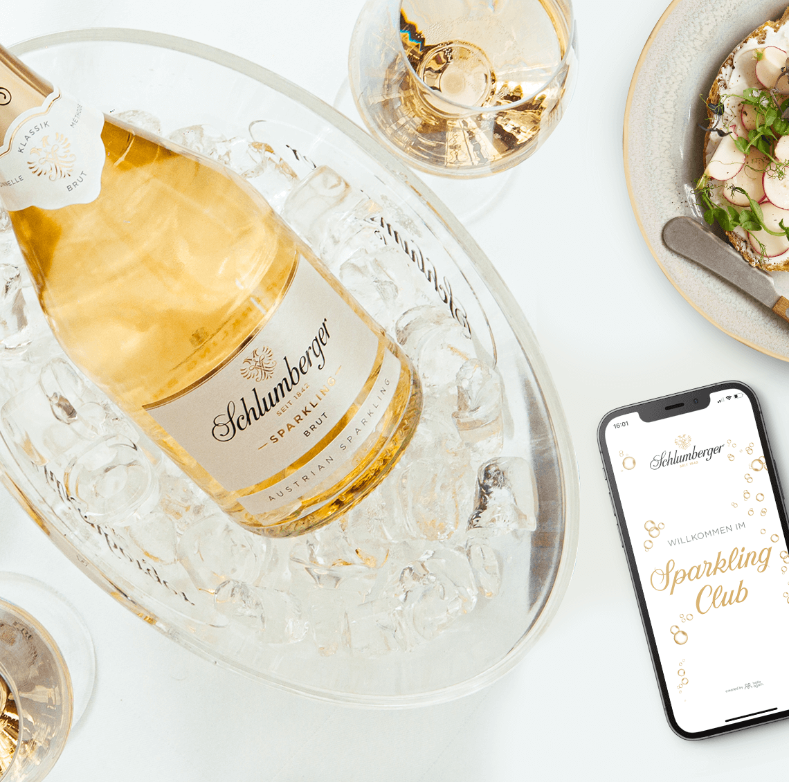 Schlumberger Sparkling Brut Klassik 0,75l Flasche im Sektkühler und Handy mit Sparkling Club App auf einen gedeckten Esstisch 