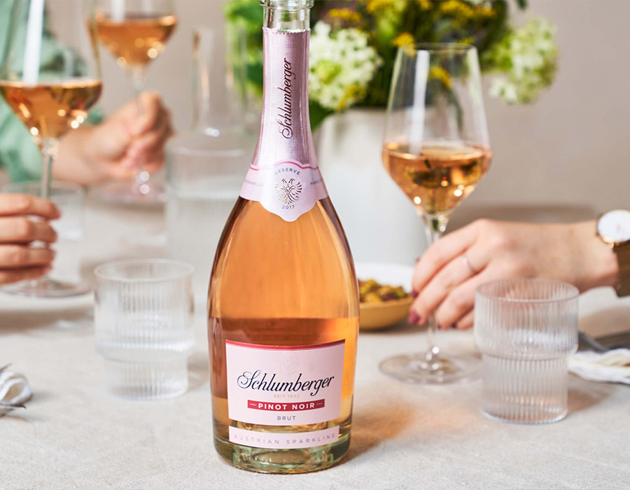 Eine Flasche Schlumberger Pinot Noir auf einem Gedeckten Tisch mit Gläsern und Händen im Hintergrund.