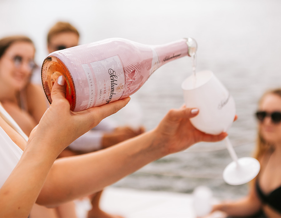 Personen sitzen am See und es wird Schlumberger Secco Rosé in ein Glas eingeschenkt.