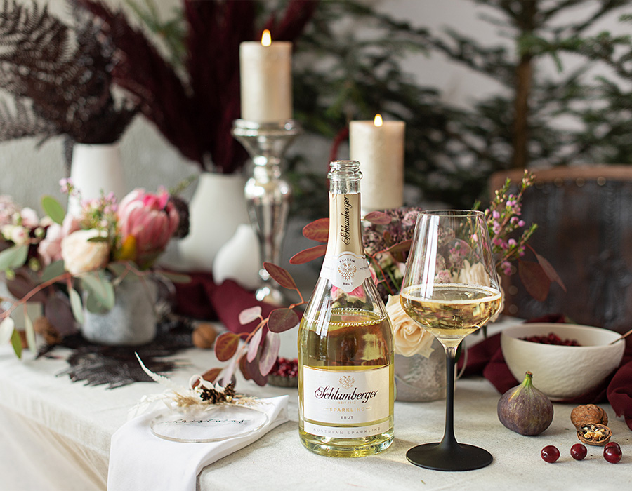 Eine Flasche Schlumberger Sparkling Brut steht auf einem mit Blumen, Kerzen und Obst gedecktem Tisch.