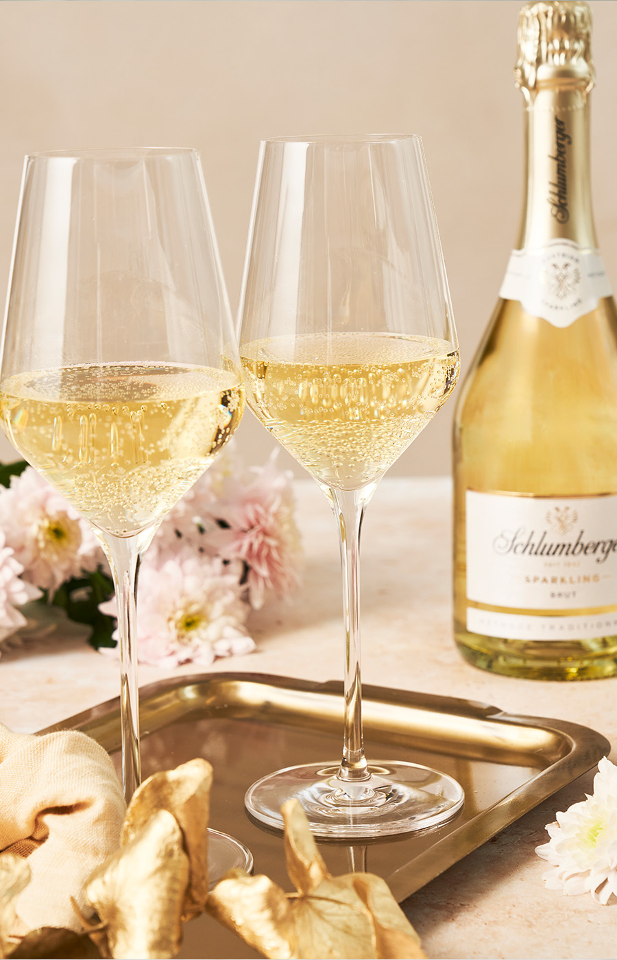 Zwei Sektgläser und eine Flasche Schlumberger Sparkling mit Blumen im Hintergrund