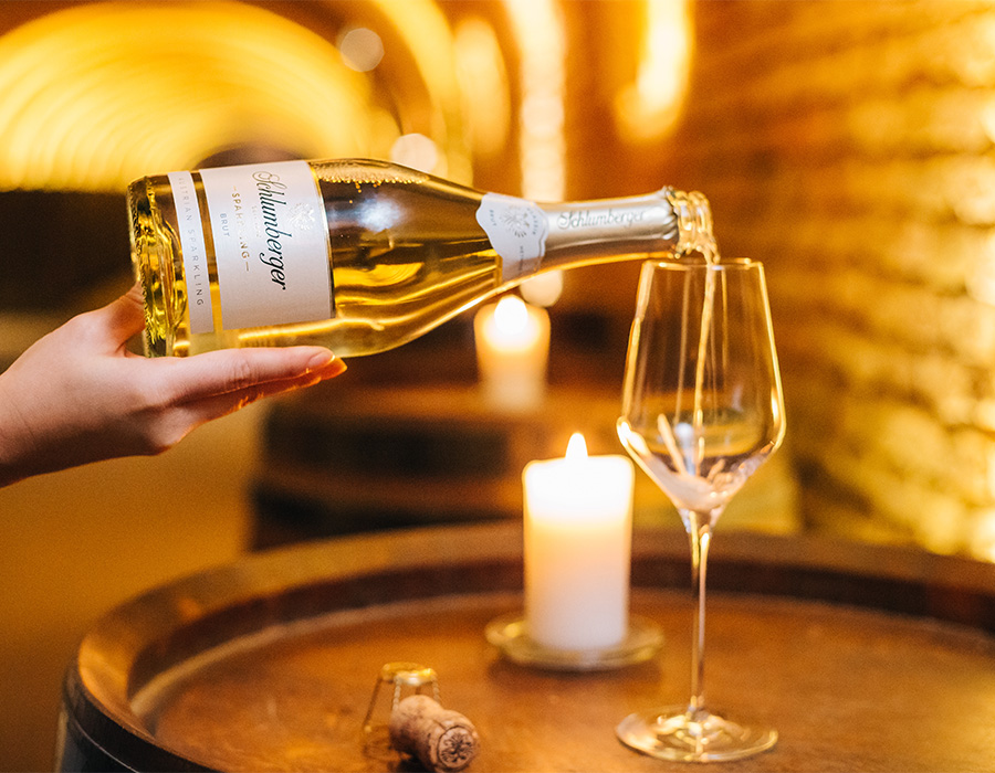Eine Hand schenkt Schlumberger Sparkling in ein Glas ein, stimmungsvolles Kerzenlicht im Hintergrund