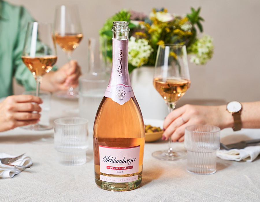 Eine Flasche Schlumberger Sekt auf einem Tisch, dahinter Personen mit Sektgläsern in der Hand
