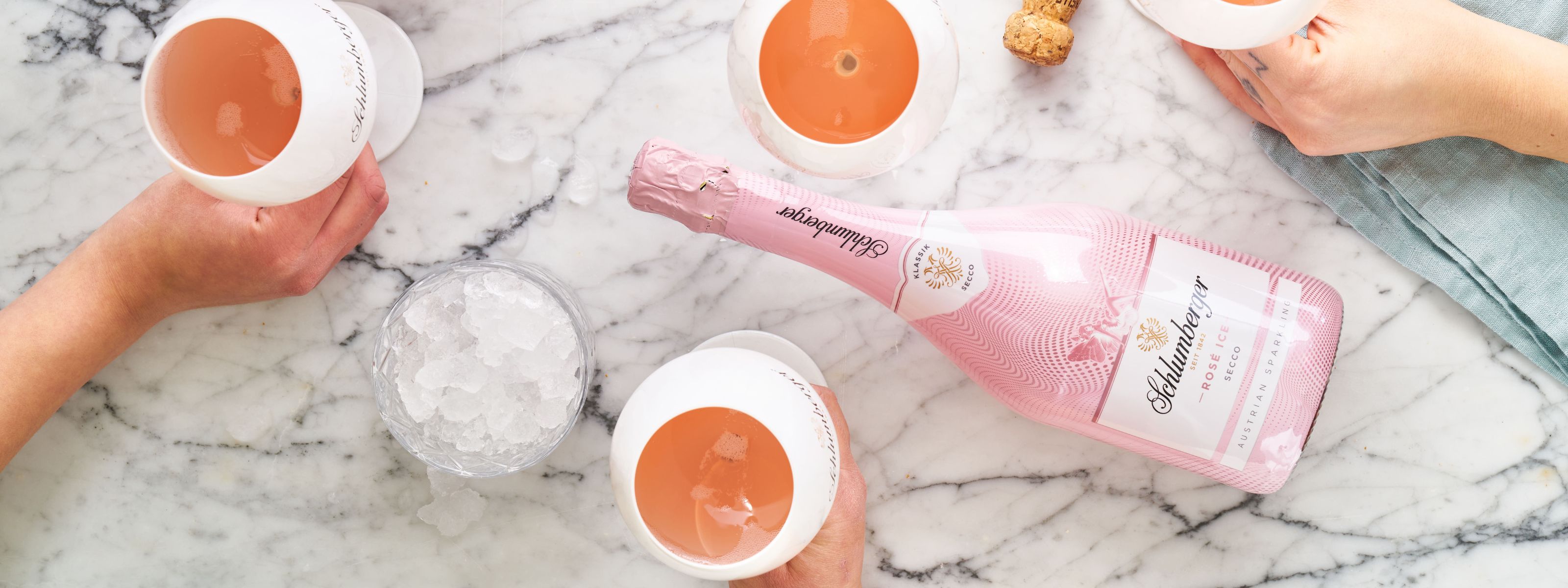 Rosé Ice Secco liegt am Mamor Tisch, daneben drei Gläser mit Sekt