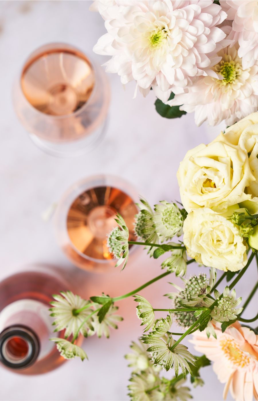 Rose Flasche und zwei gefüllte Gläser stehen am Tisch mit Blumen