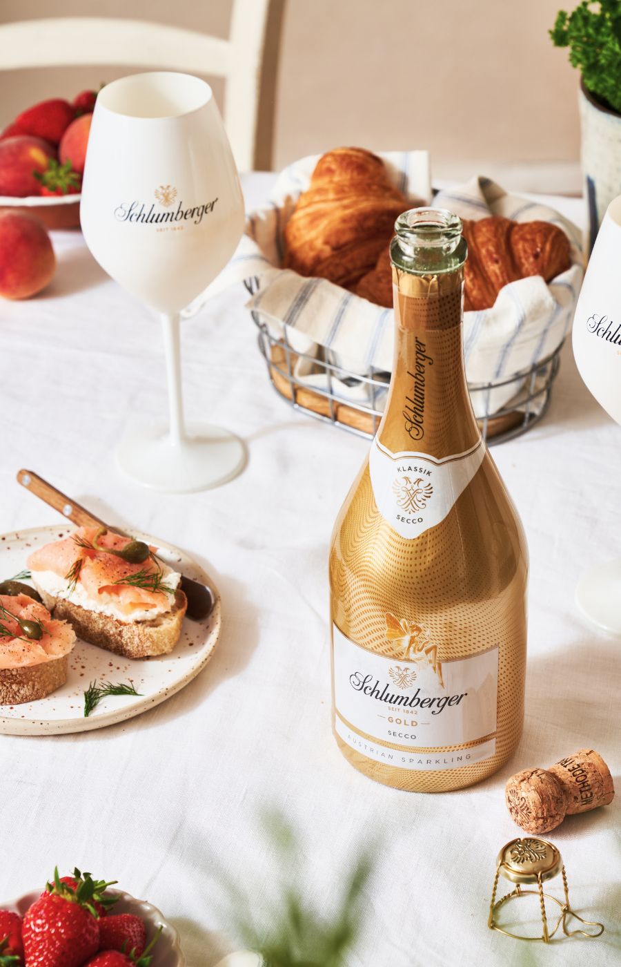 Frühstückstisch mit Lachsbrötchen, Croissants, Obst und Goldsecco