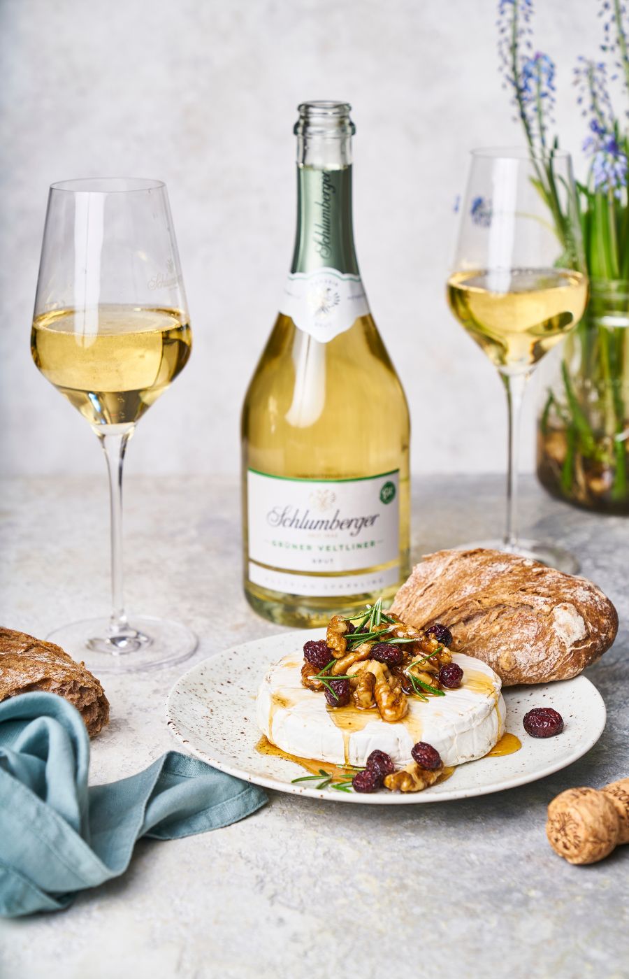 Grüner Veltliner Schaumweinflasche,zwei gefüllte Weingläser und ein Ziegnkäse mit Honig steht am Tisch.