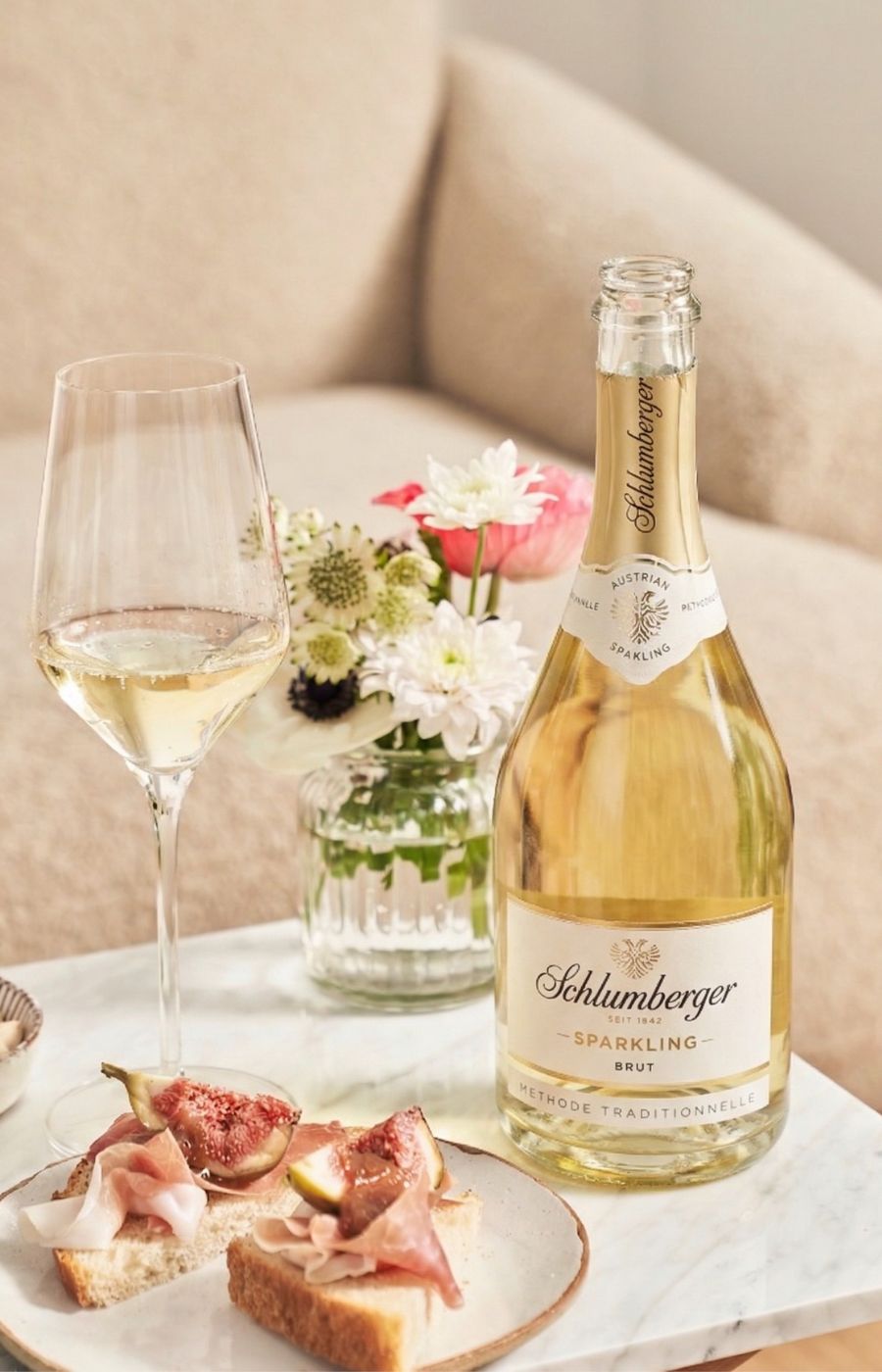 Couchtisch mit eienr Flasche Sparkling Brut, einem gefülltem Glas und zwei Prosciutto Brötchen