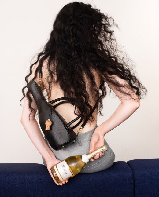 Dame mit nacktem Rücken trägt Tasche und hält Flasche in der Hand