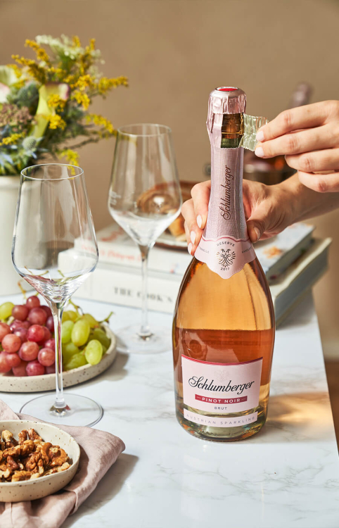 Gedeckter Tisch mit Walnüssen und Trauben, zwei Sektgläsern und einer Flasche Schlumberger Sekt, die geöffnet wird.