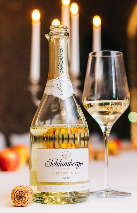 Eine geöffnete Flasche Schlumberger Sparkling Brut mit einem Glas Sekt im Kerzenschein.
