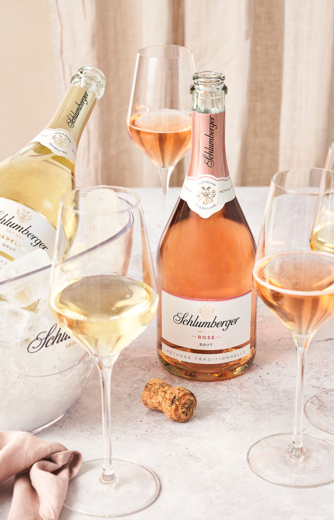 Sektgläser und eine Flasche Schlumberger Sekt auf einem Tisch, daneben eine Flasche in einem Kübel mit Eis