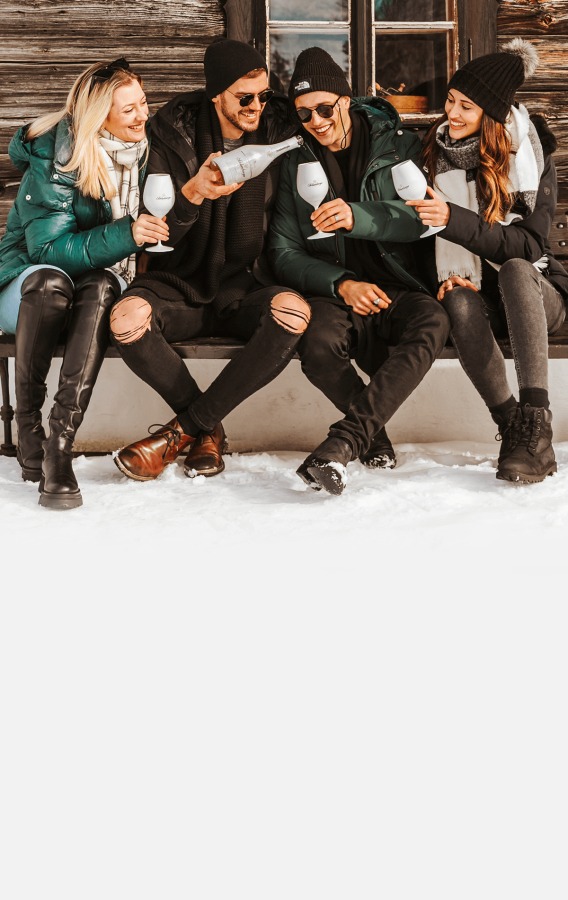Gruppe junger Leute beisammen vor einer winterlichen Almhütte mit einer Flasche Schlumberger White Ice Secco.