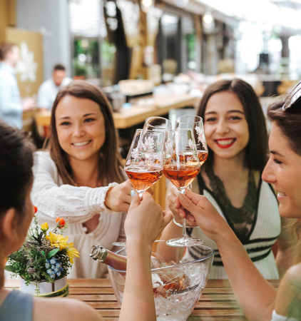 Damen stoßen im Gastgarten mit ein Glas Rosé Sekt