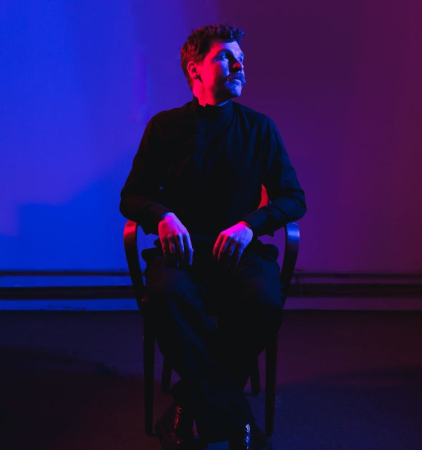 Kunst fon O. Ablinger Mann sitzt am Stuhl und ist blau und violett beläuchtet