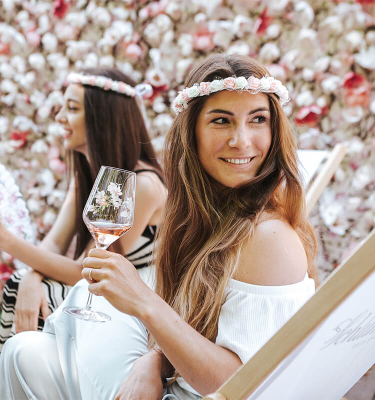 Dame sitzt mit Glas Schlumberger Rosé im LIegestuhl vor einer Blumenwand