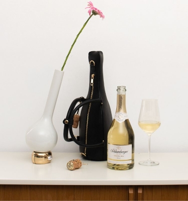 Schwarze Tasche steht auf Kommode mit einer Flasch sparkling einem Glas und einer Blume