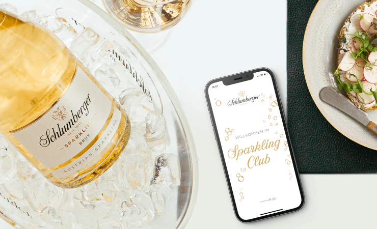 Schlumberger Sparkling Brut Klassik 0,75L Flasche im Sektkühler und Handy mit Sparkling Club App auf einen gedeckten Esstisch 