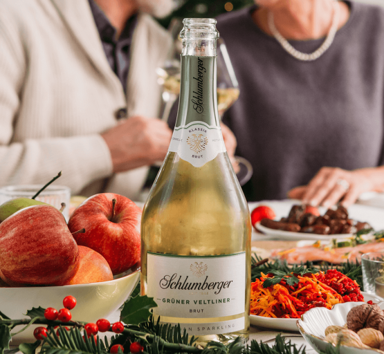 Schlumberger Grüner Veltliner 0,75L Flasche steht auf einem gedeckten Tisch mit zwei Personen im Hintergrund