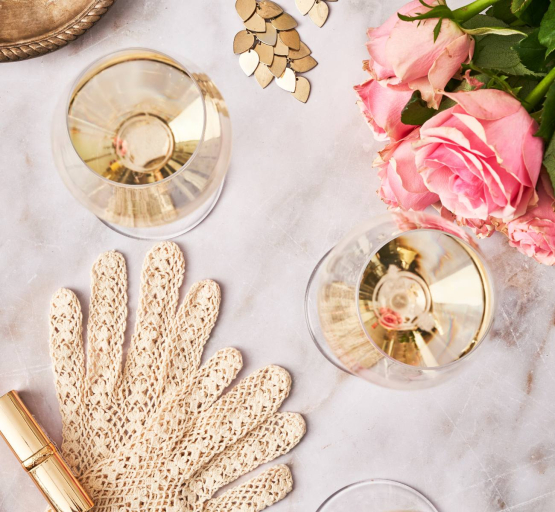 Zwei Gläsermit Sekt stehen auf einem Tisch mit Rosen, Handschuhe und einem Lippenstift