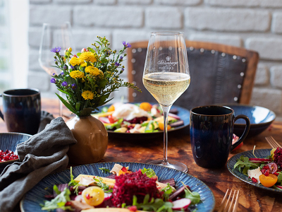 Ein Glas Schlumberger Sekt auf einem Tisch gedeckt mit Salat, Blumen und Tassen