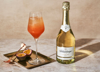 Sektcocktail Rezept in Weinglas auf Tablett mit Flasche Sparkling und Passionsfrucht daneben