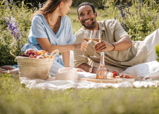 Ein Paar sitzt auf einer Picknickdecke und stoßt mit Rosé an