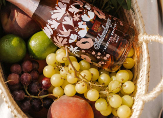 Flasche steckt im Picknick-Korb mit Blumen und Obst und einer Käseplatte