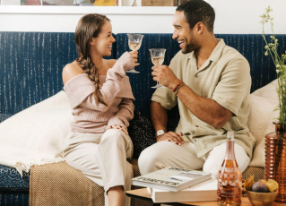 Pärchen sitzt auf blauer Couch und stoßt mit Rosé an